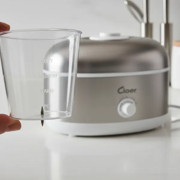 Cloer electronic egg boiler with its measuring cup and integrated egg piercer visible on a kitchen counter.